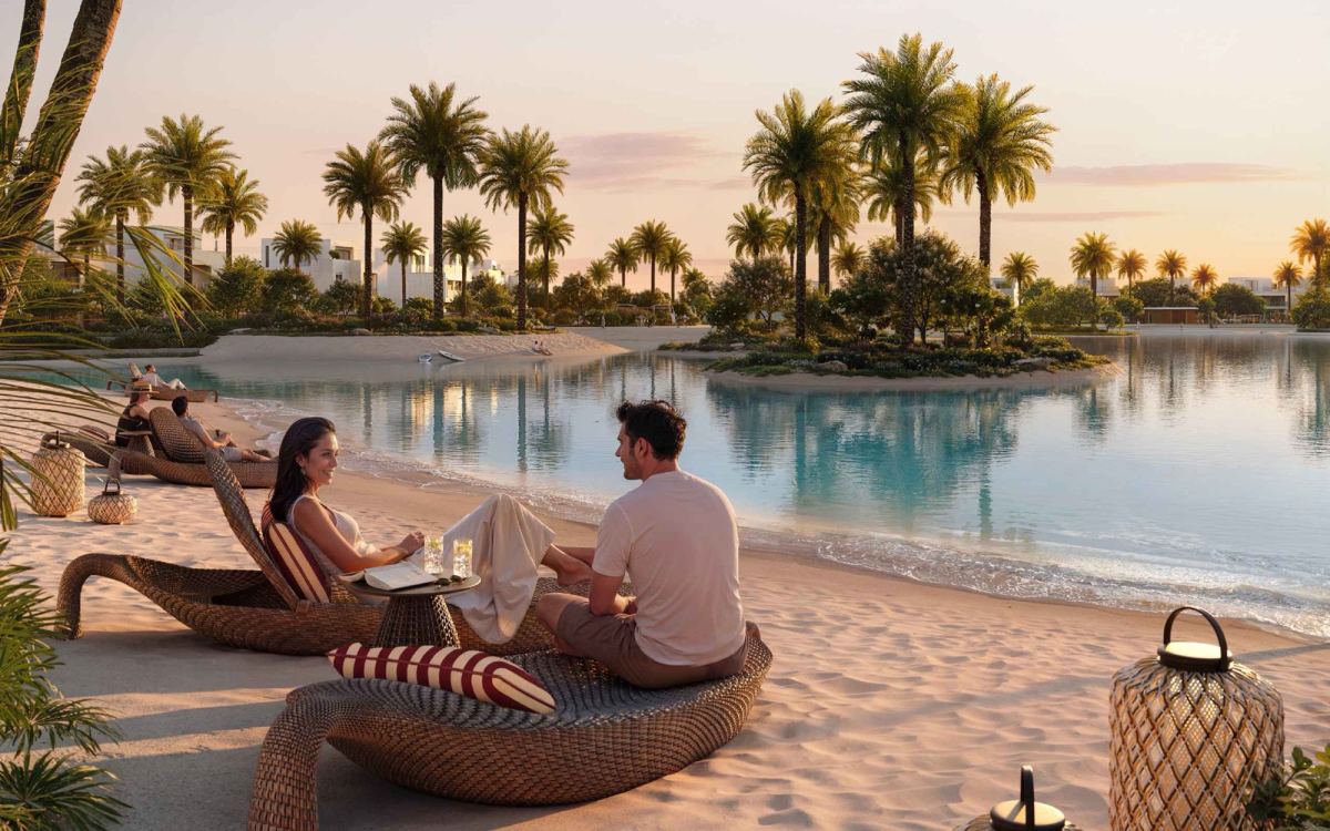 Residents relaxing on loungers beside the private beach and lagoon at The Heights Country Club & Wellness by Emaar at sunset.