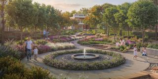 A circular fountain and flowering planting in a park at Sobha Sanctuary, with families walking the paths.